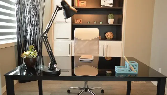 Büroumzug Heidenheim. Ein Glas-Schreibtisch mit Tischlampe, Blumentopf und Kalender, begleitet von einem Bürostuhl und einem Regal mit Büchern und Pflanzen, nach einem Büroumzug mit A2B Umzüge.